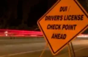 orange dui sobriety and drivers license checkpoint ahead sign along side of road with car light trails in background